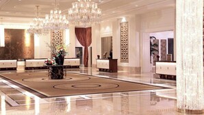 A spacious lobby with multiple reception desks, large chandeliers, and decorative columns.