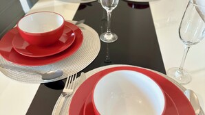Uma mesa de jantar posta com pratos vermelhos e brancos, talheres e copos de vinho, com um jogo de mesa preto.