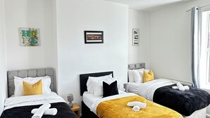 Quarto de hotel com duas camas, carpete cinzento, paredes brancas e uma pintura de uma paisagem urbana.