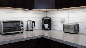 A kitchen with a toaster, a coffee maker, and a kettle on a granite countertop. - Stylish Modern Family Suite with Patio (Toronto)