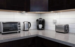Una cocina con tostadora, cafetera y hervidor sobre una encimera de granito.
