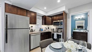 A modern kitchen with stainless steel appliances, dark wood cabinets, and a dining area with a table set for two. - Stylish Modern Family Suite with Patio (Toronto)