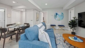 Una sala de estar moderna con un sofá azul, una mesa de comedor para cuatro personas y un cuadro abstracto grande en la pared.