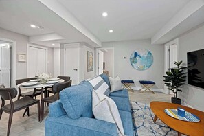 Una sala de estar moderna con un sofá azul, una mesa de comedor para cuatro personas y un cuadro abstracto grande en la pared.