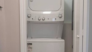 A laundry room with a front-loading washer and dryer, a wicker basket, and a door leading to another room. - Stylish Modern Family Suite with Patio (Toronto)