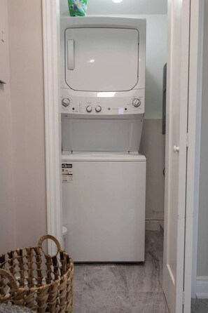 Un lavadero con lavadora y secadora de carga frontal, una cesta de mimbre y una puerta que da a otra habitación.