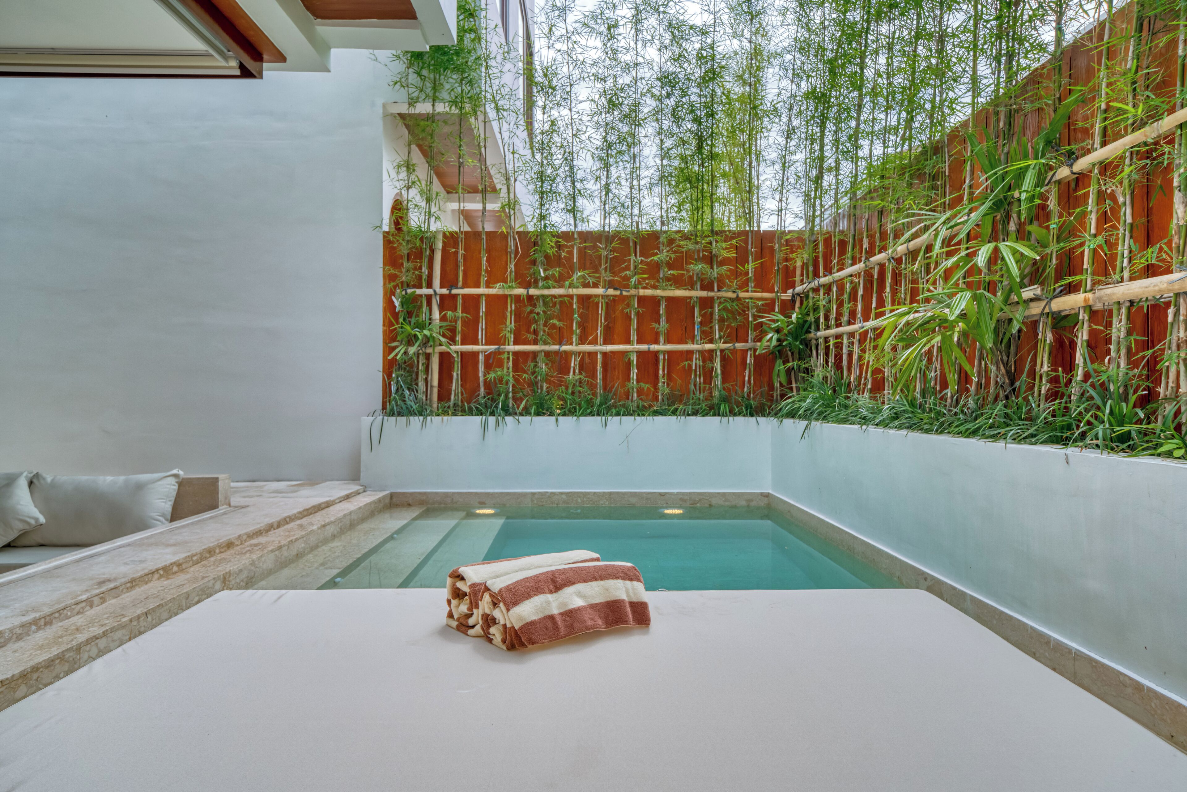 A pool area with a bamboo fence, a white lounge chair, and a towel on a table.