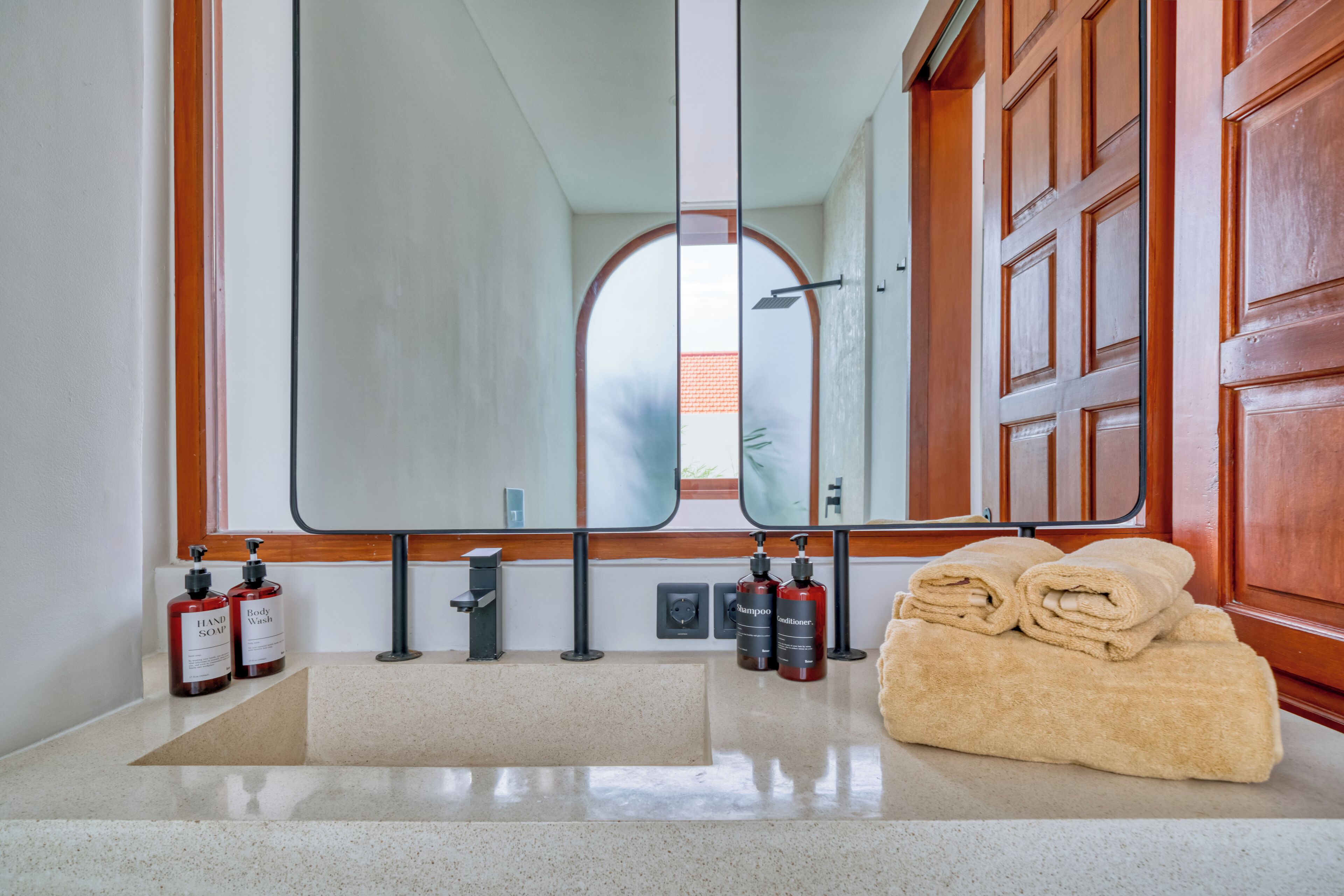 A bathroom with a large mirror, wooden cabinets, a sink with a soap dispenser, and a towel stack.