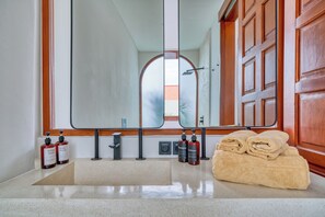A bathroom with a large mirror, wooden cabinets, a sink, and a towel stack.