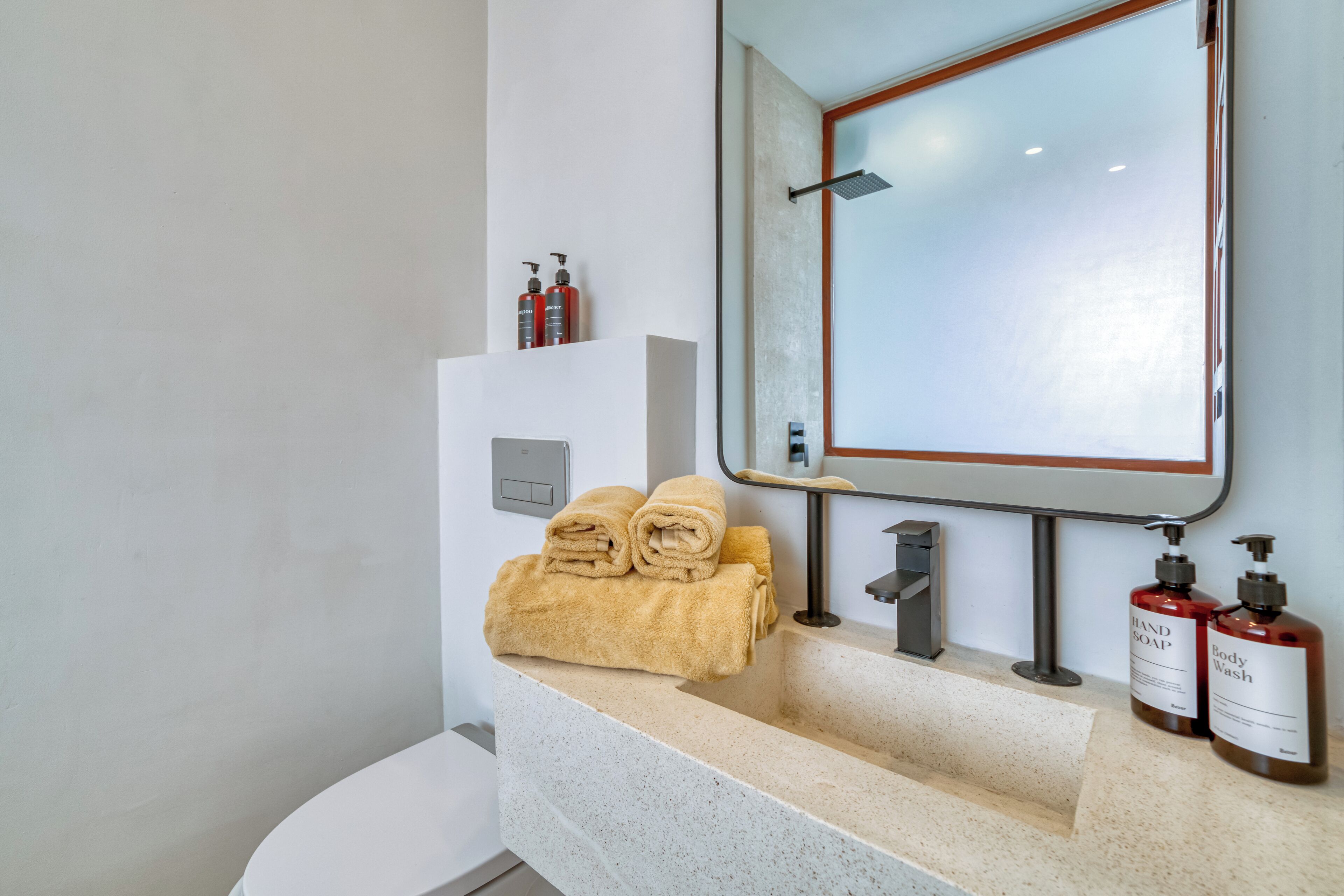 Un baño con un lavamanos blanco, un espejo y dos botellas de jabón de manos y gel de ducha.