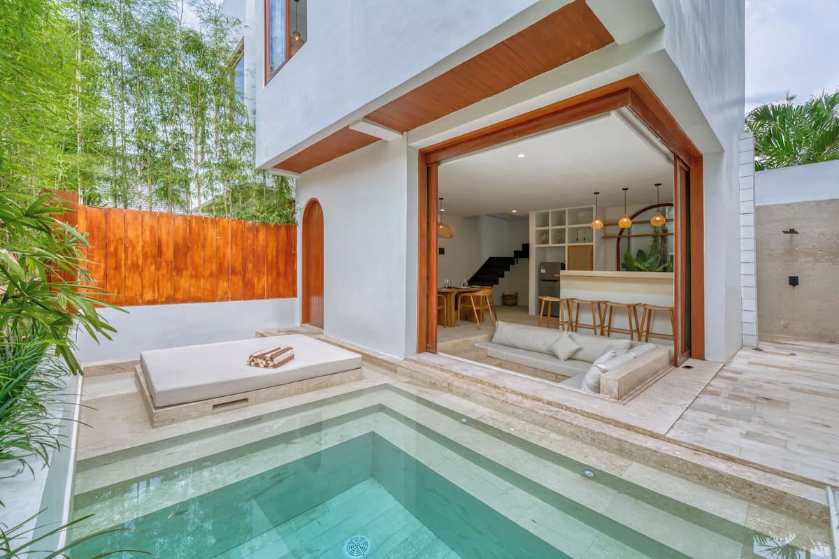 A modern outdoor pool area with a wooden deck, a lounge chair, and a dining area with a table and chairs.