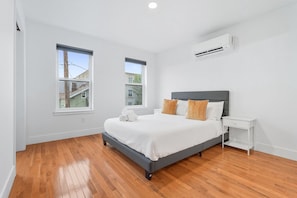A bedroom with a bed, two windows, an air conditioner, and a nightstand.