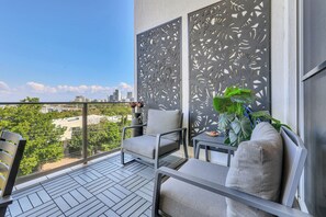 A balcony with a city view, a chair, a small table, and a decorative panel.