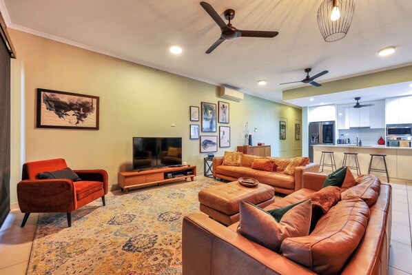 A living room with a sofa, a television, and a kitchen in the background.
