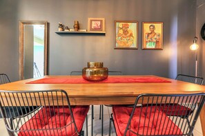 Uma área de refeições com uma mesa de madeira, almofadas vermelhas, cadeiras de metal e obras de arte na parede.