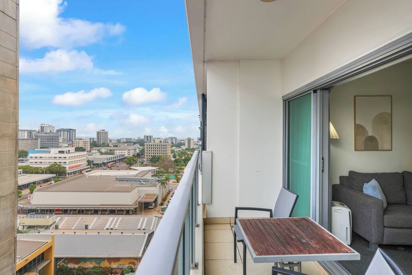 Ein Balkon mit Blick auf die Stadt, ein graues Sofa und ein Holztisch.