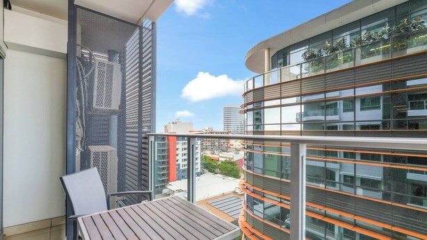 A balcony with a table and chairs, overlooking a modern building with glass windows and orange accents.