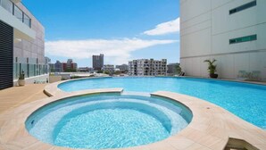 A rooftop swimming pool with a hot tub, surrounded by modern buildings and a clear sky.