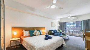 A hotel room with a large bed, a sofa, a small table, and a balcony with a view.
