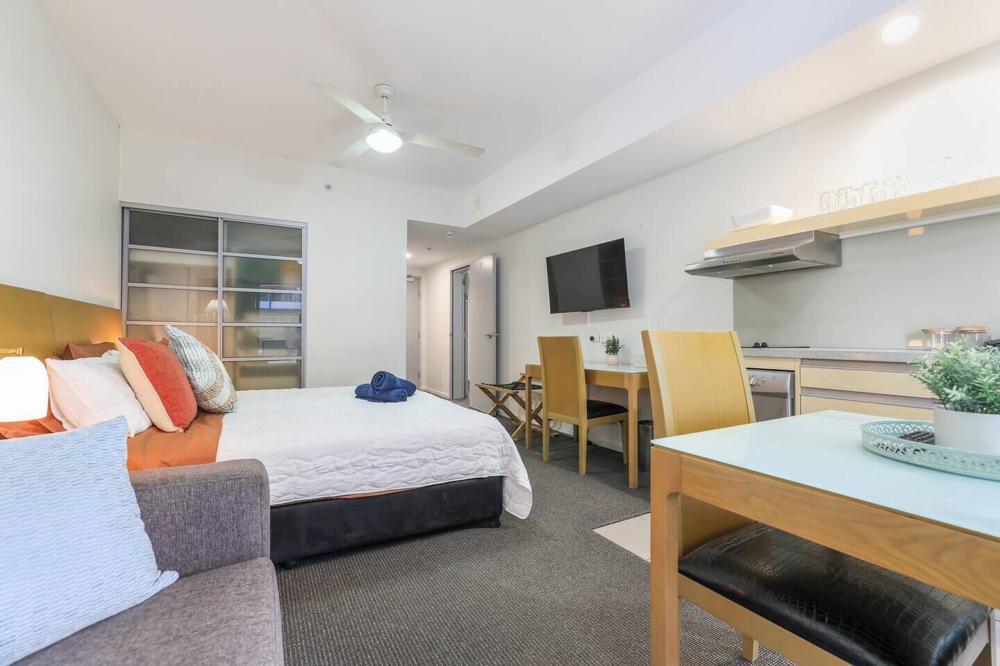Ein Hotelzimmer mit Bett, Schreibtisch, Stuhl, Fernseher und einer Küchenzeile.