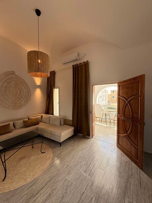 A modern living room with a sectional sofa, a hanging light fixture, and a view of the outside. - Luxury accommodation in the city center (Houmt Souk)