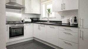A modern kitchen with white cabinets, a stainless steel range hood, a built-in oven, a sink, and a window with a plant. - Modern Cotswolds lakeside retreat, spa and pool (Somerford Keynes)