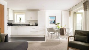 A modern kitchen with white cabinets, a dining area with a table and chairs, and a sofa. - Modern Cotswolds lakeside retreat, spa and pool (Somerford Keynes)