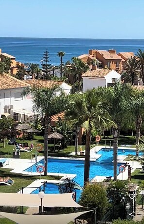 A resort with a swimming pool surrounded by palm trees and a view of the ocean. - Premium apartment 300 meters from the sea, 5G Wi-Fi, private parking, swimming pool. (Manilva)