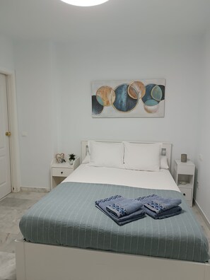A bedroom with a bed, white nightstands, a wall art piece, and a folded towel on the bed. - Premium apartment 300 meters from the ocean, 5G Wi-Fi, private parking, pool. (Manilva)