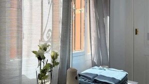 Una habitación con una cama, una ventana con cortinas y un jarrón con flores.