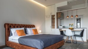 Een moderne slaapkamer met een gestoffeerd hoofdeinde, een groot bed en een werkhoek met stoelen.