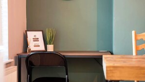 A room with a wooden desk, a black chair, a wooden table, a framed menu, and a potted plant.