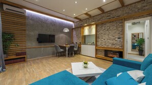 A modern living room with a fireplace, a dining area, and a kitchen with a brick wall. - Sapphire - Max Luxury Apartments, a Large Apartment in the Belgrade City Center (Beograd)