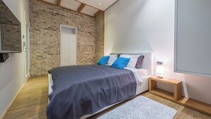 A bedroom with a bed, a nightstand, a lamp, a white door, and a brick wall. - Sapphire - Max Luxury Apartments, a Large Apartment in the Belgrade City Center (Beograd)