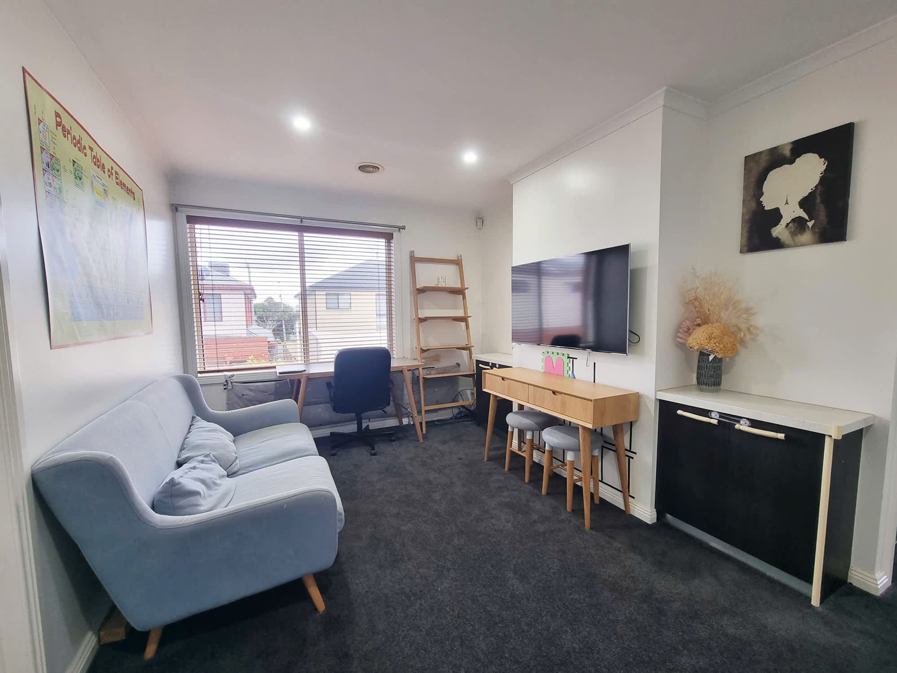 A modern living room with a grey sofa, a wooden desk, a TV, and a painting on the wall.