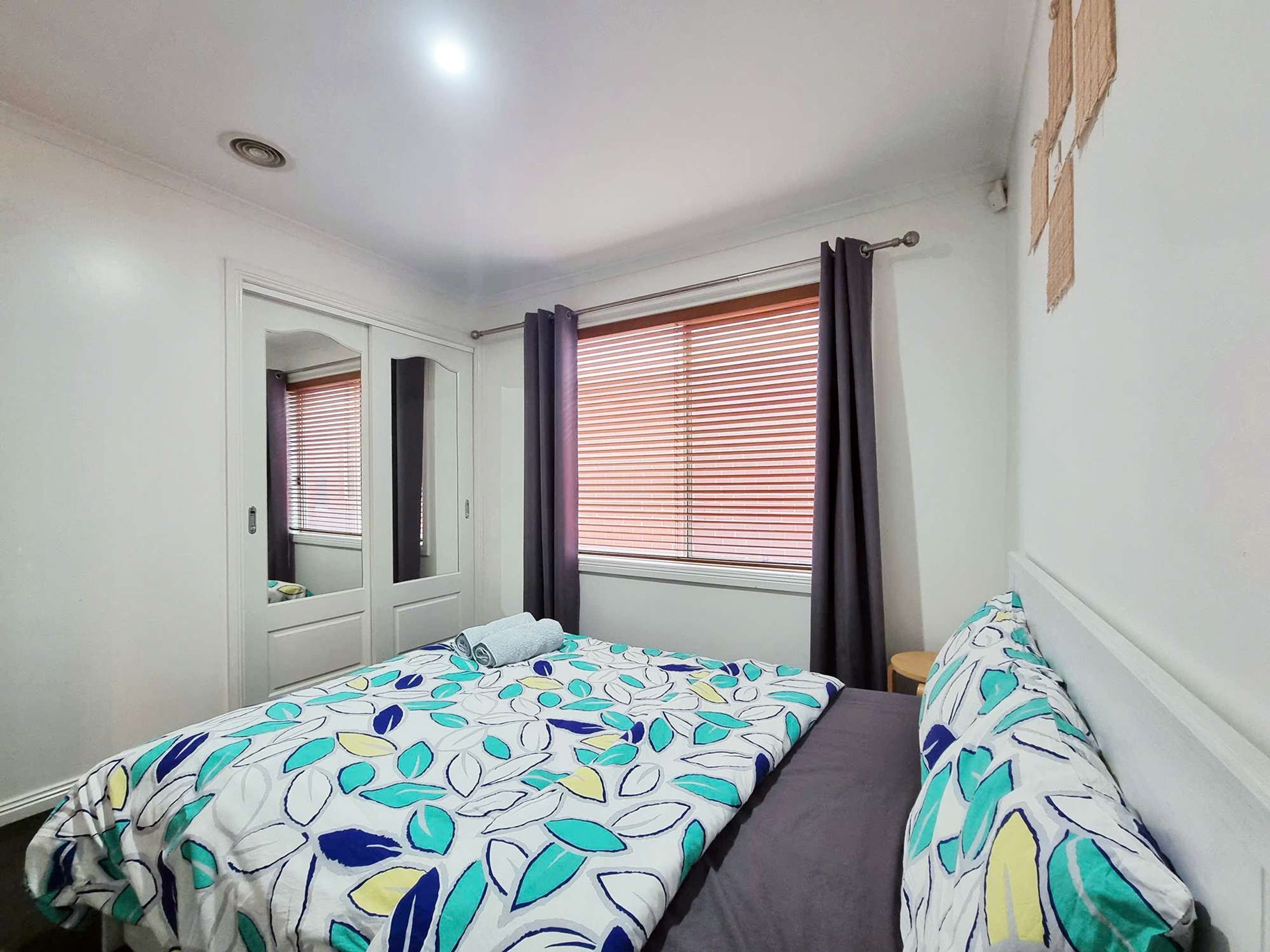 Een slaapkamer met een bed, een kledingkast en een raam met gordijnen.
