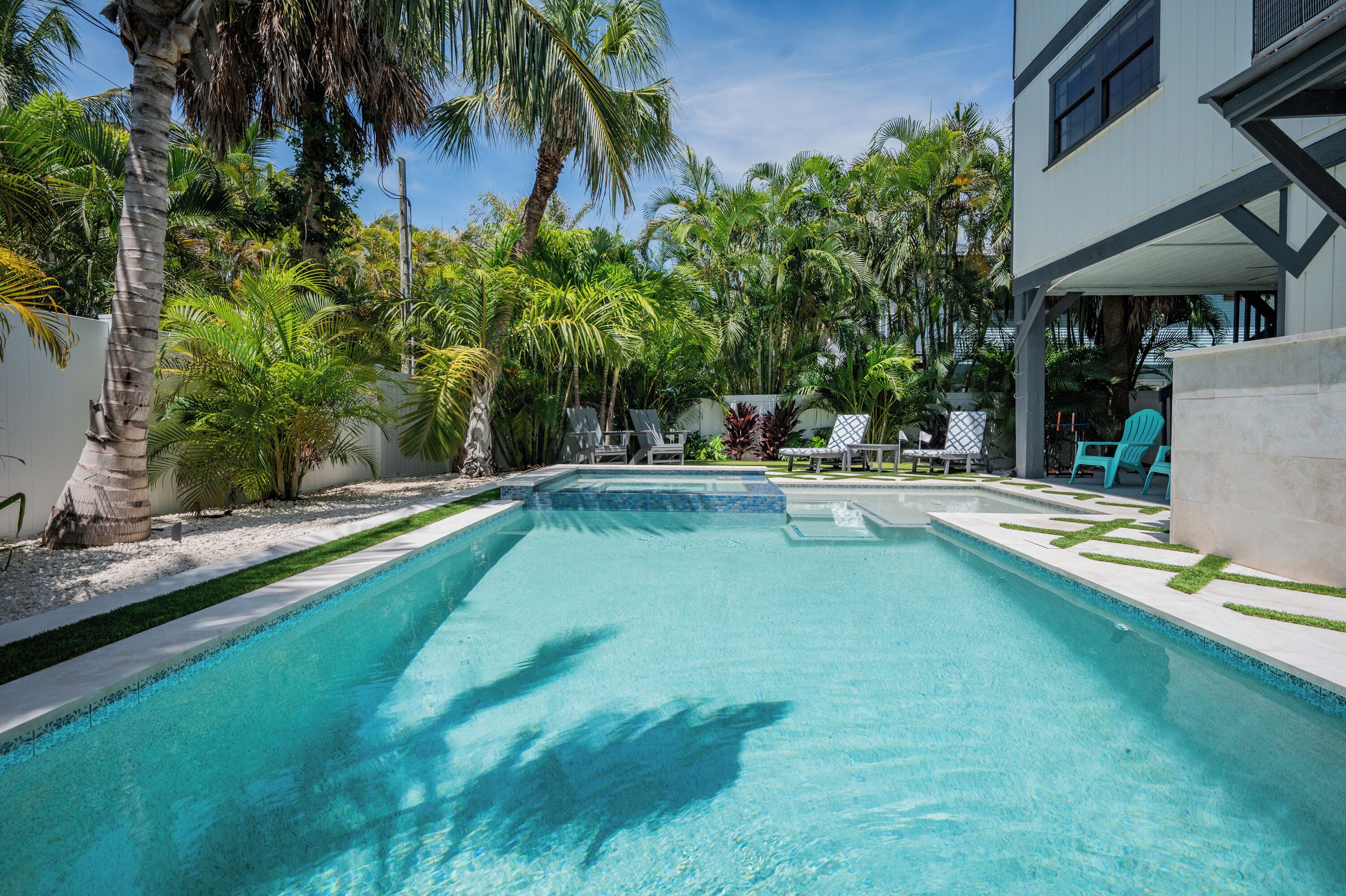 A swimming pool with clear blue water, surrounded by palm trees and a white building with a balcony.