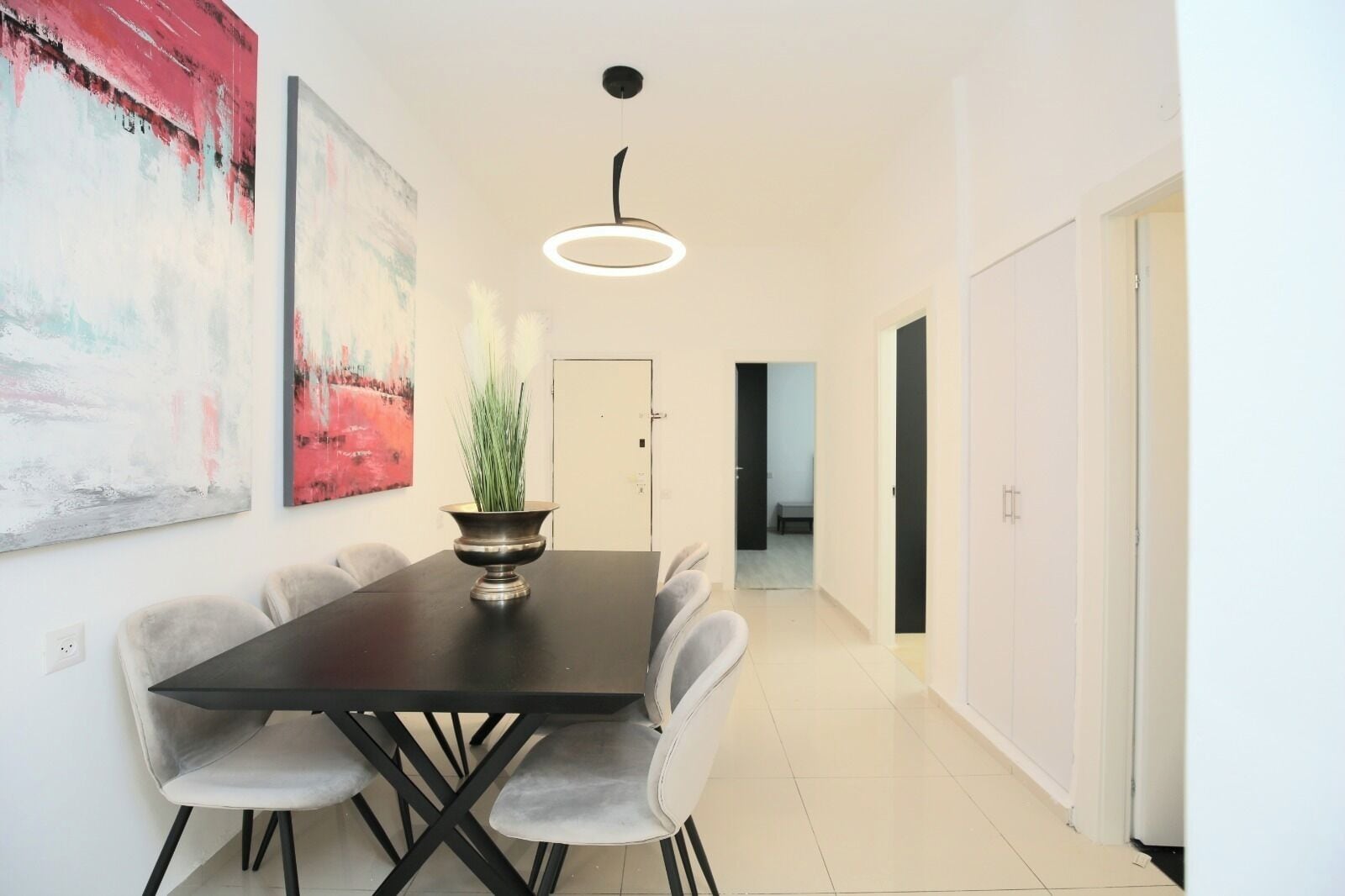 Un comedor moderno con una mesa de madera oscura, cuatro sillas tapizadas de gris, un cuenco decorativo de metal con follaje y una lámpara colgante.