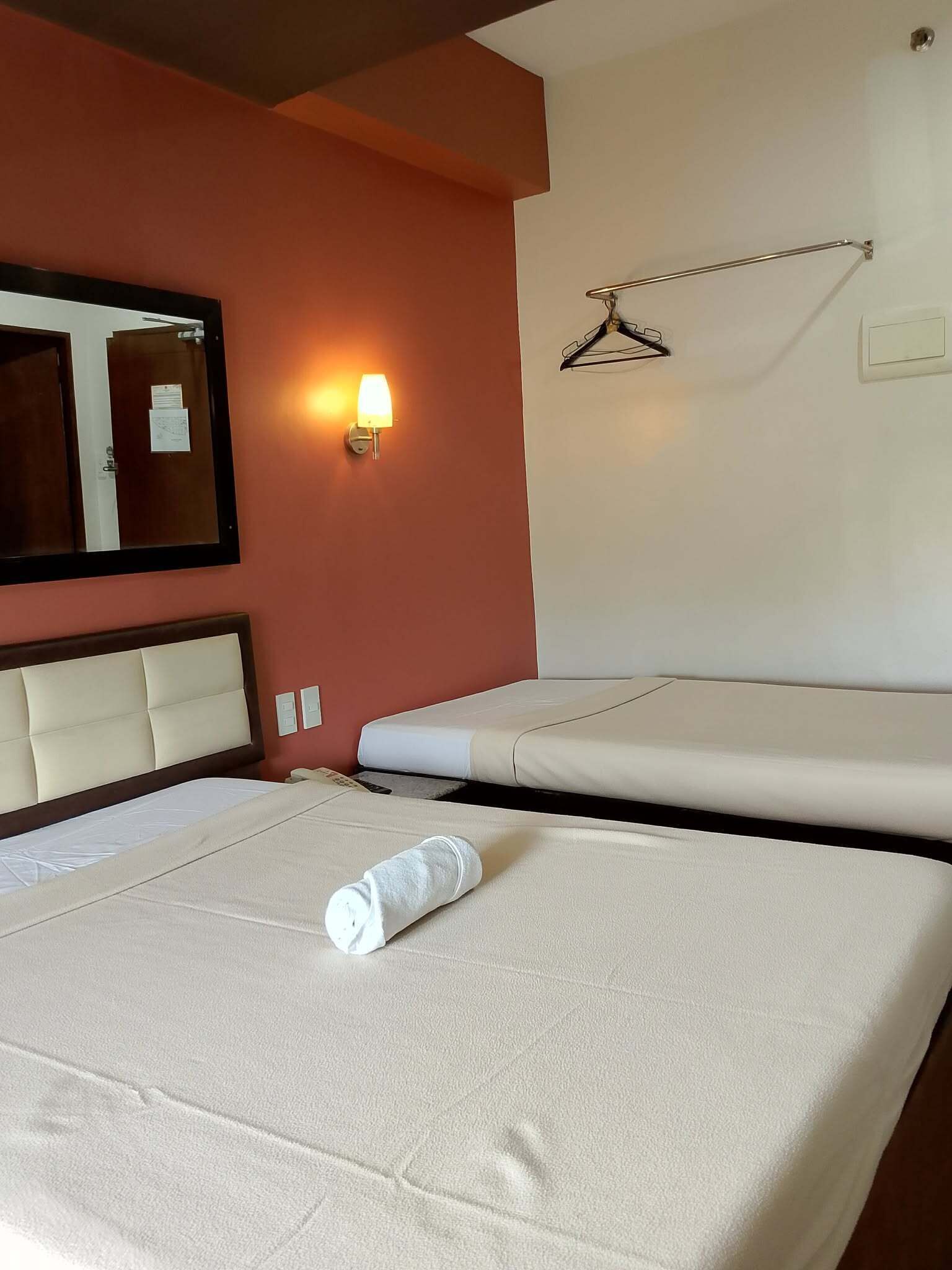 Hotellihuone, jossa on kaksi sänkyä, suuri peili, seinään kiinnitetty valaisin ja naulakko.