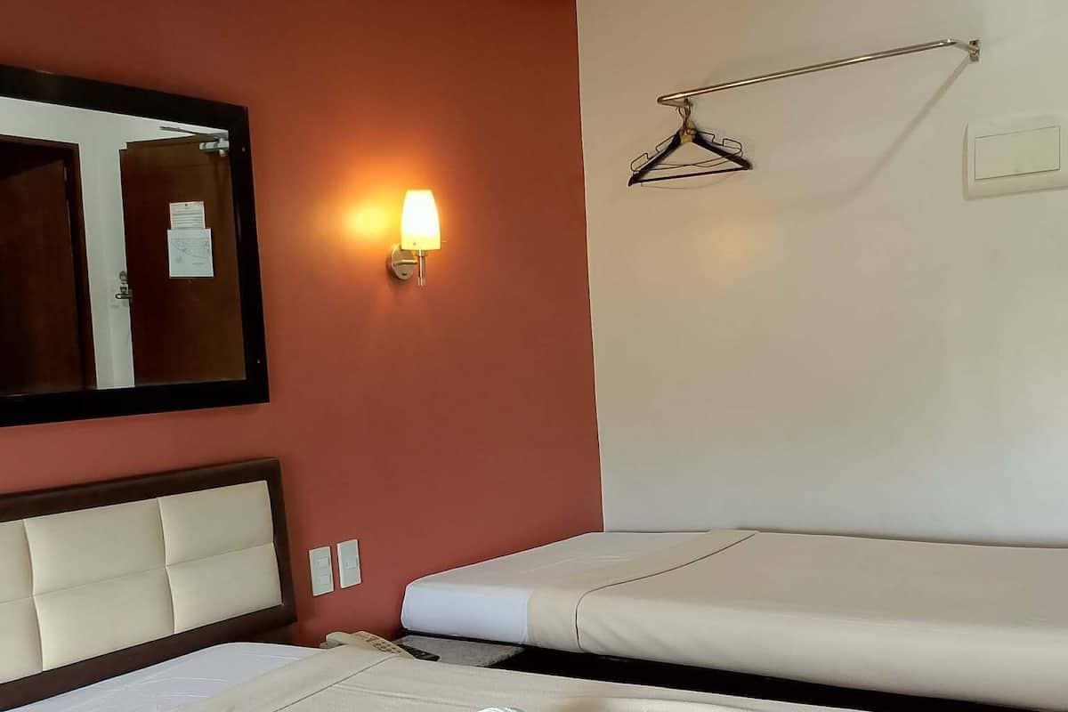 Hotellihuone, jossa on kaksi sänkyä, suuri peili, seinään kiinnitetty valaisin ja naulakko.