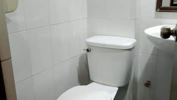 A small, white-tiled bathroom with a white toilet and a sink.