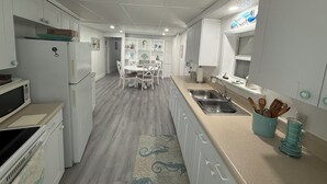 Cocina compacta con armarios blancos, una mesa de comedor con sillas, microondas, refrigerador y pileta.
