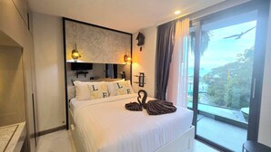 A hotel room with a large bed, a flat-screen TV, a clock, and a view of the city through large windows. - A204 - 1 Bdr Condo With Sea View, Ao Nang Beach (Krabi)