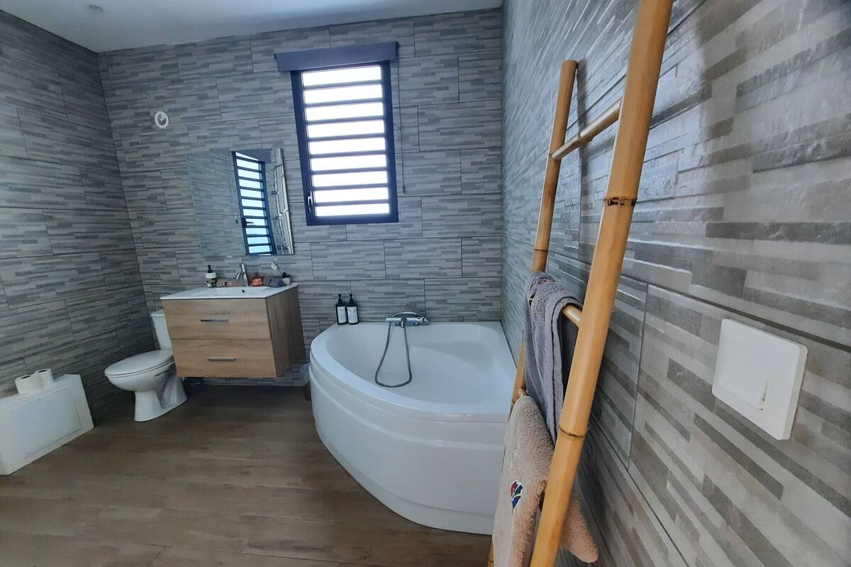 Ein modernes Badezimmer mit einem Holzwaschtisch, einer freistehenden Badewanne und einem Fenster mit Jalousien.