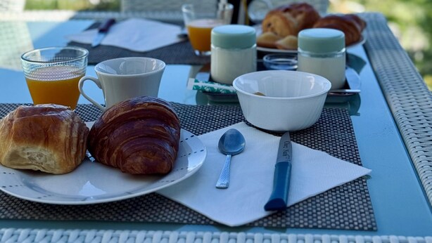 Une table de petit-déjeuner avec des croissants, un verre de jus d’orange et une vue sur l’océan.