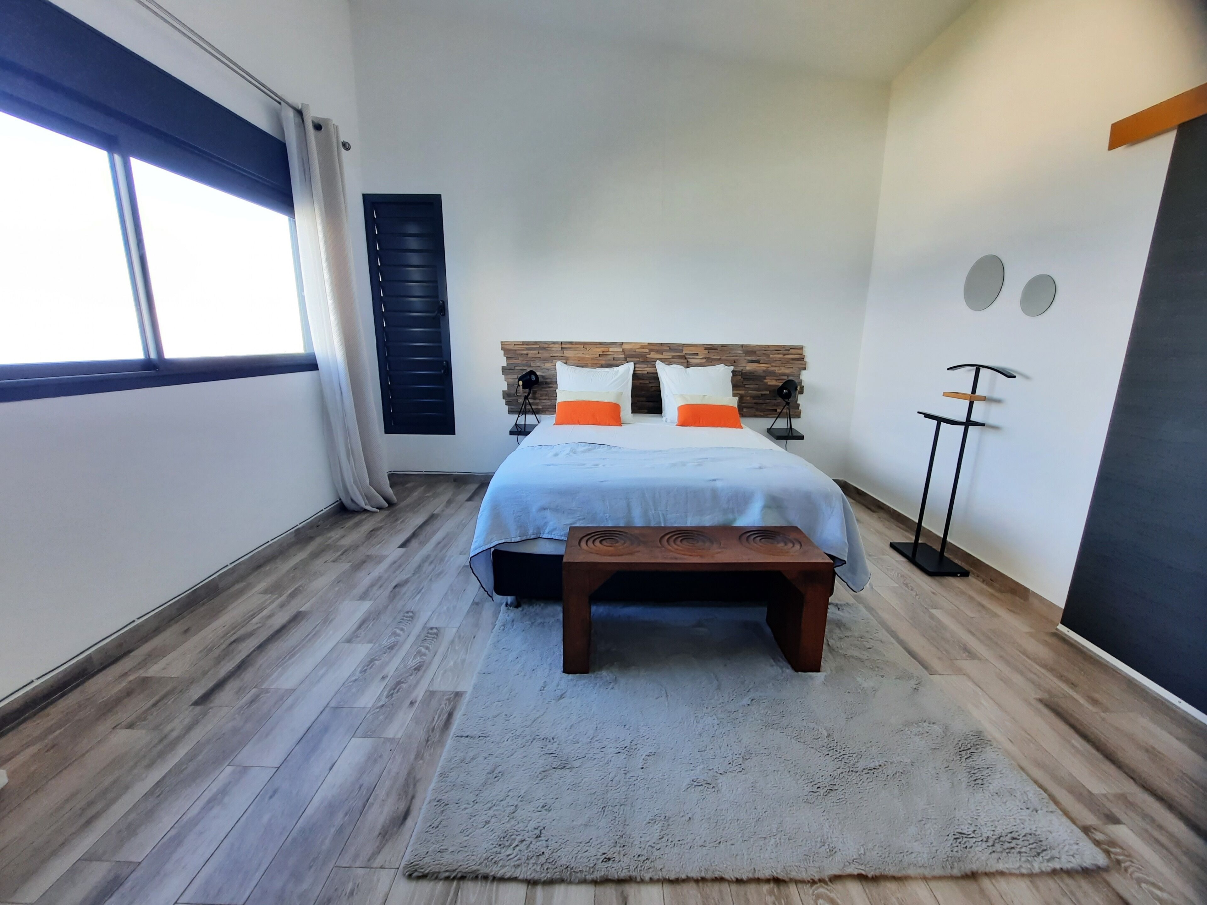 A bedroom with a bed, bedside table, and a standing fan.