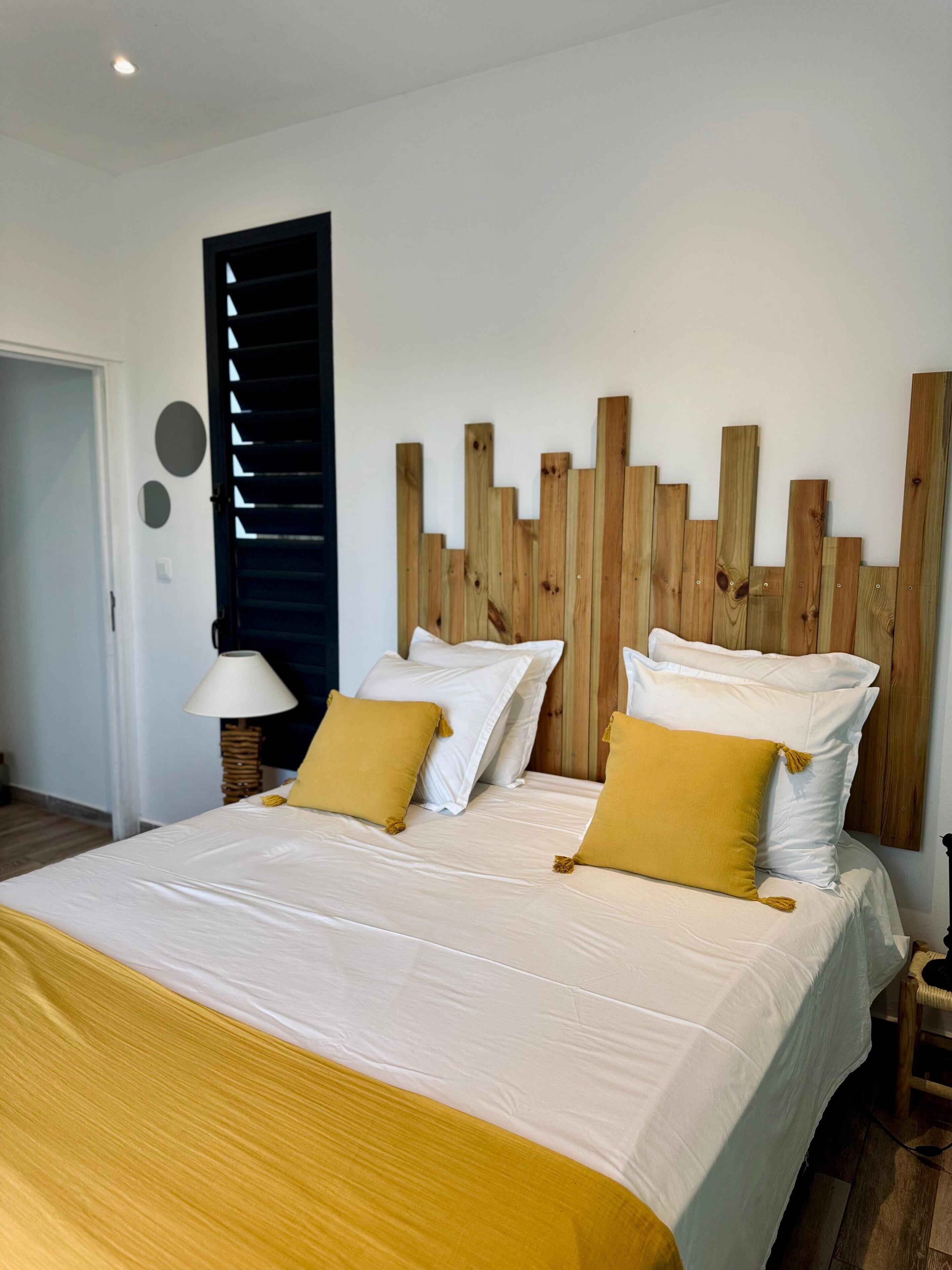 A bedroom with a bed, white bedding, wooden headboard, and a lamp.