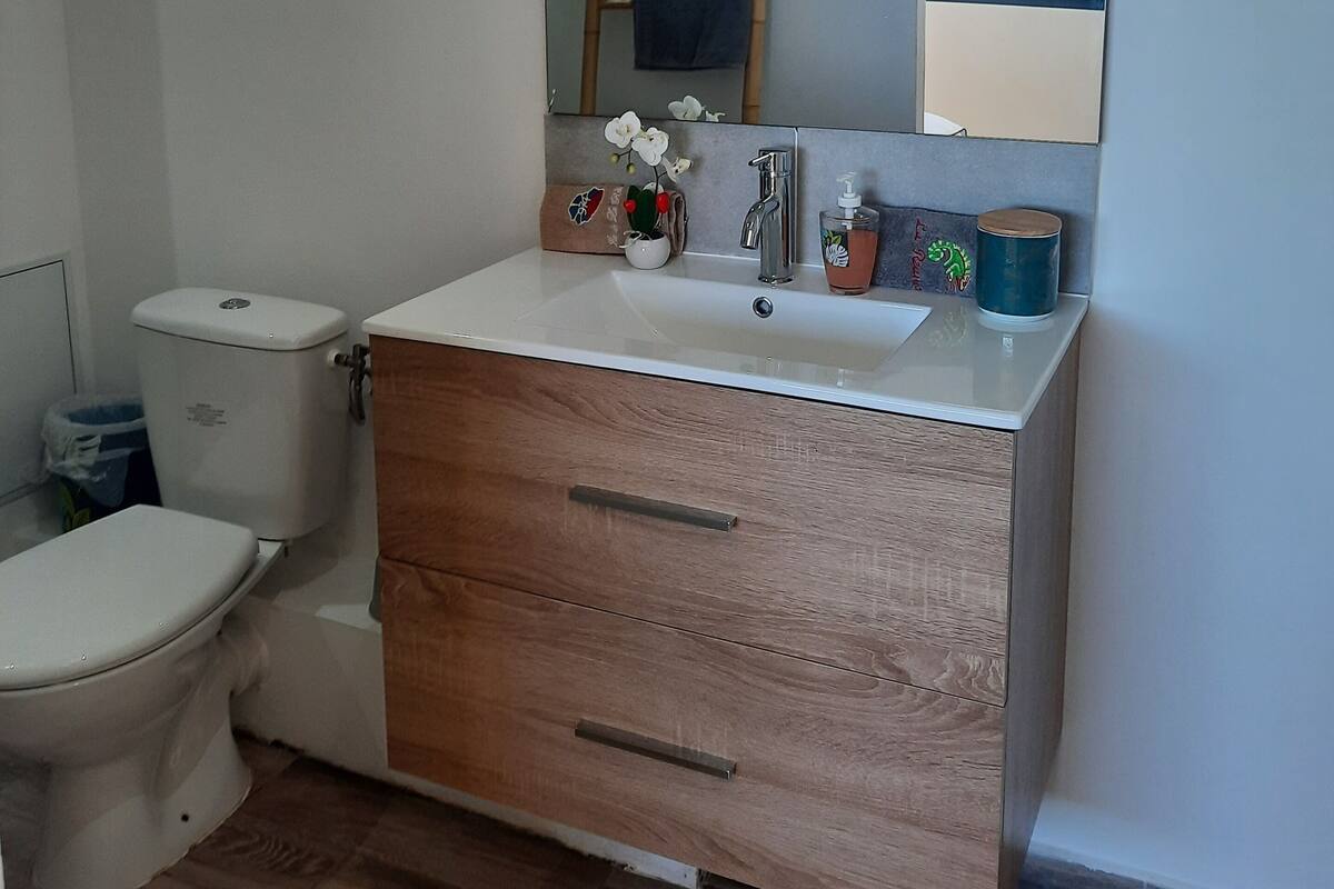 Ein Badezimmer mit Toilette, Waschbecken und einem Spiegel darüber sowie einem Holzkorpus darunter.
