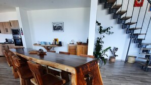 Une cuisine moderne avec des meubles en bois, un four encastré et un coin repas comprenant une grande table et des chaises en bois.