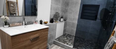 Een moderne badkamer met een houten wastafelmeubel, een grote spiegel, een douchecabine en een betegelde vloer.